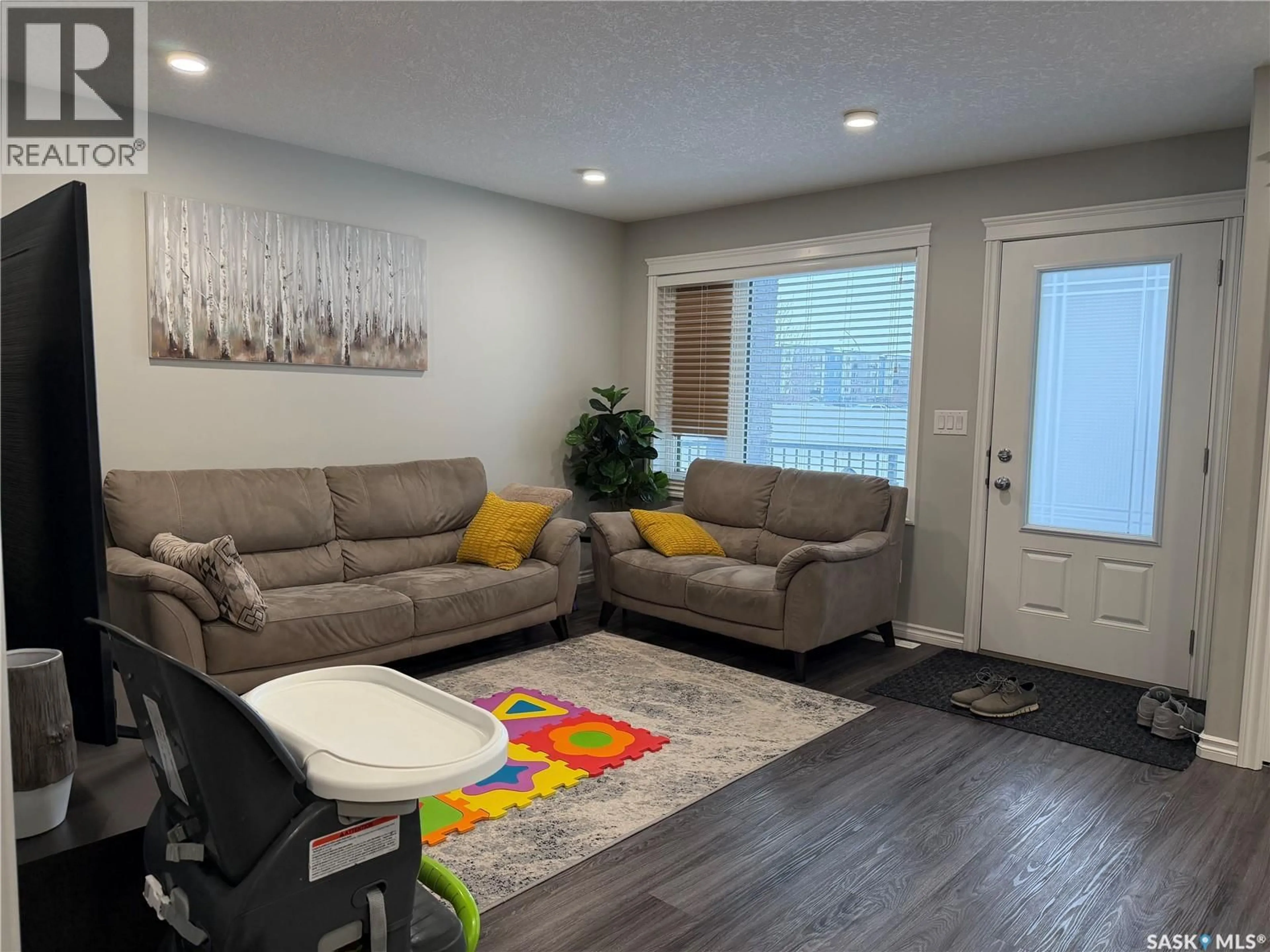 Living room with furniture, wood/laminate floor for 201 110 AKHTAR BEND, Saskatoon Saskatchewan S7W0Y9